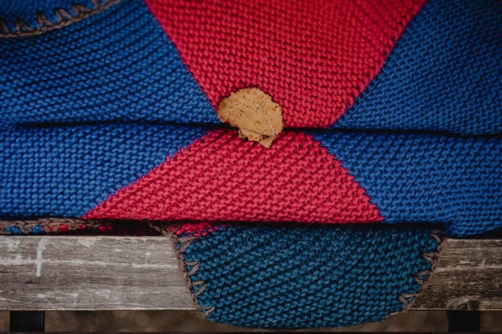 Mastering the First Impression: Your intriguing post title goes here Handmade knitted blanket in vibrant red and blue featuring a fallen leaf on a wooden bench.